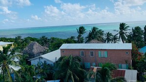 A coastal view with a building featuring a red facade and green shutters, surrounded by lush greenery and palm trees. - Laguna Hotel (San Pedro)