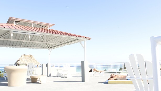 A beachside lounge with a covered seating area, a thatched-roof structure, and a view of the sea. - Laguna Hotel (San Pedro)