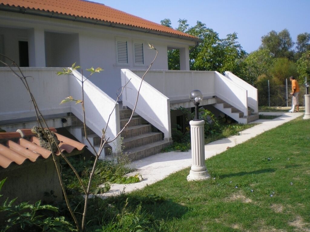 A white building with a red-tiled roof, a staircase, and a small garden area.