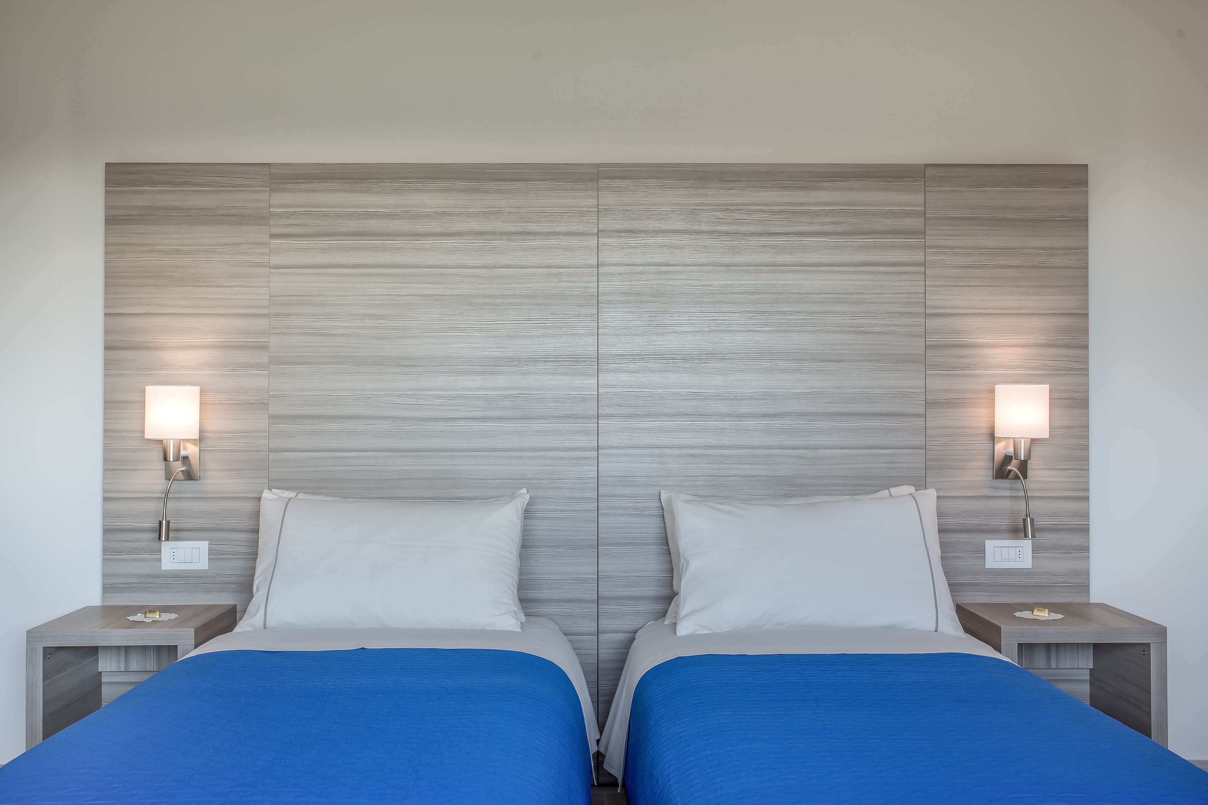 Una cama doble con colcha azul, dos mesitas de noche con lámparas y un cabecero de madera.