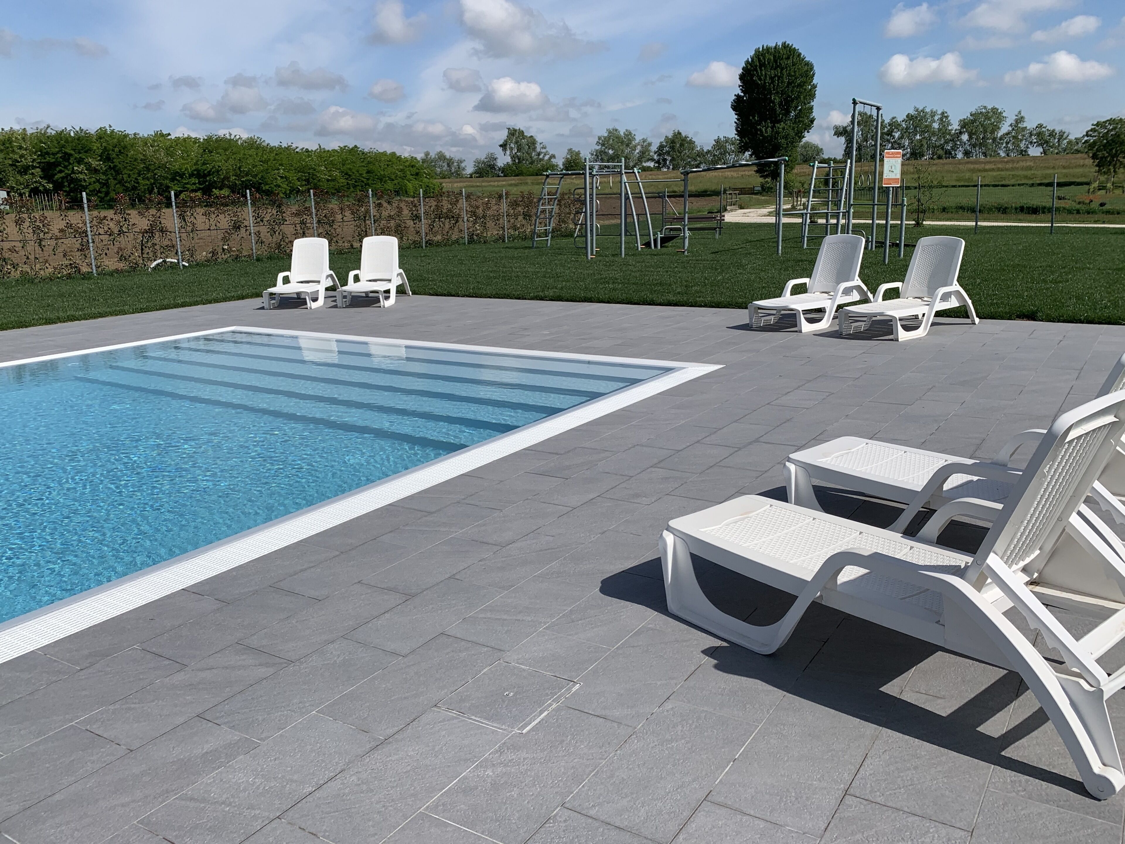 Une piscine entourée de chaises longues blanches et d’une terrasse dallée.
