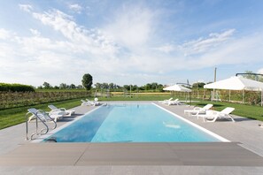 A rectangular swimming pool with a clear blue water surface, surrounded by white lounge chairs and a covered seating area. - Country House Campofiore (Pontelongo)