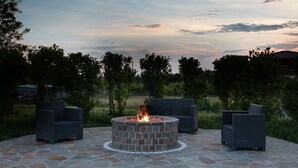 A stone fire pit surrounded by wicker chairs in an outdoor setting. - Country House Campofiore (Pontelongo)