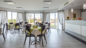 A dining area with multiple tables and chairs, large windows with curtains, and a view of the outdoors. - Country House Campofiore (Pontelongo)