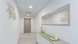 A hallway with a light-colored wooden floor, a white wall with a decorative leaf pattern, a mirror with a leaf design, and a counter with a green mat and candles. - Country House Campofiore (Pontelongo)