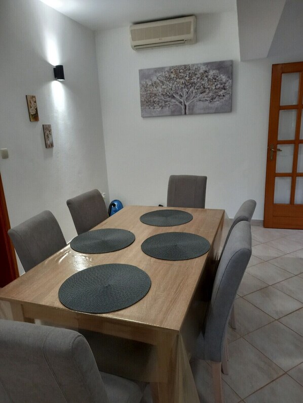 A dining area with a wooden table, four grey chairs, and a wall-mounted air conditioner.