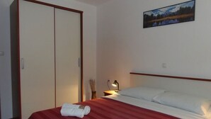 A hotel room with a bed, a nightstand, a lamp, a painting on the wall, and a wardrobe. - Apartment in Dramalj with Seaview, Balcony, Air condition, WIFI (4623-12) (Dramalj)