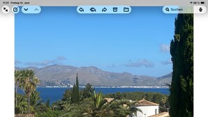 Un paisaje costero con un edificio blanco, palmeras y montañas al fondo.