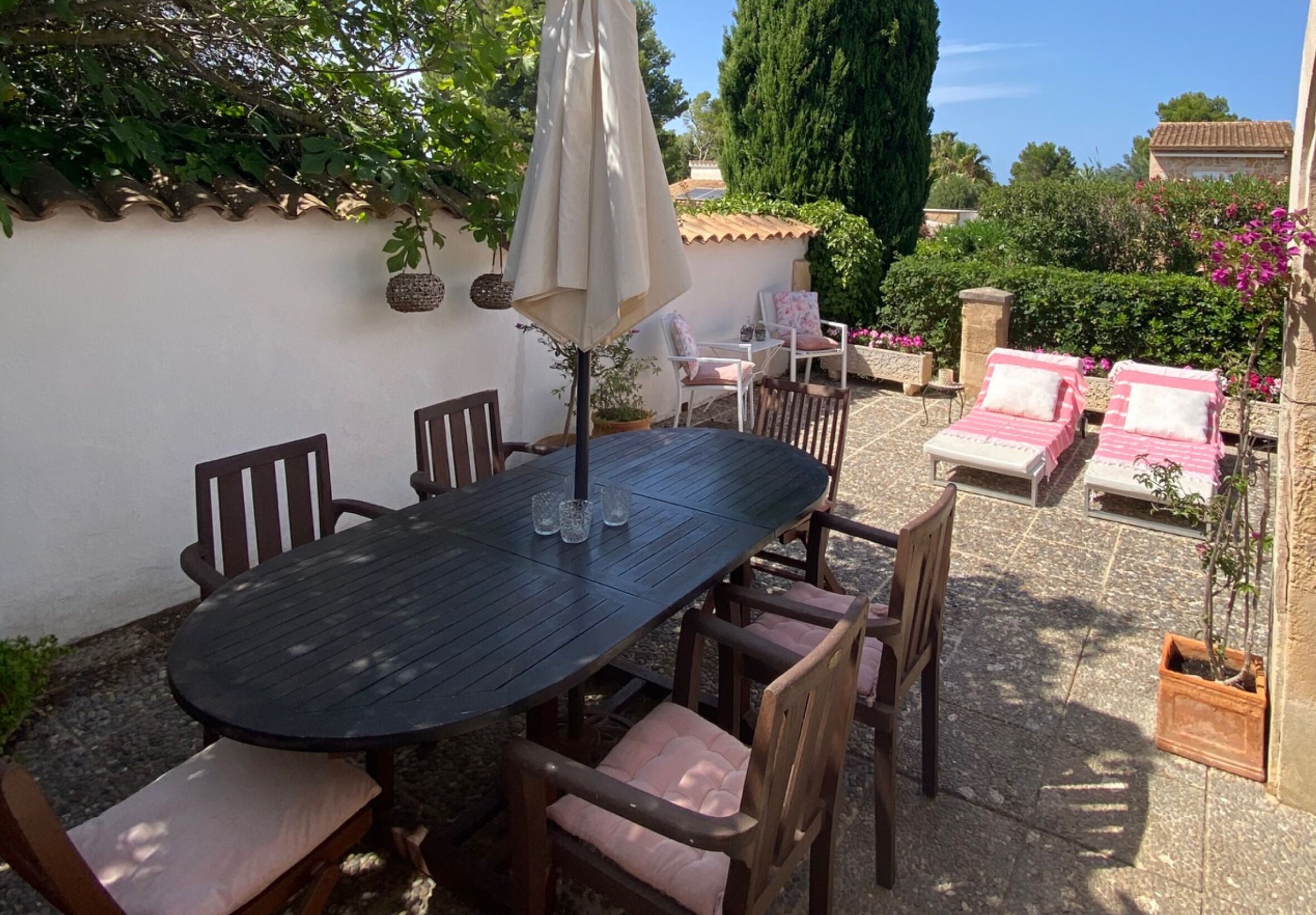 Une terrasse extérieure avec une table ronde et des chaises, entourée de plantes en pot et d’un espace détente avec des fauteuils.