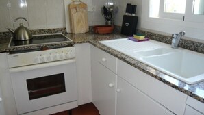 Una cocina compacta con armarios blancos, un horno empotrado, una tetera de acero inoxidable y una encimera de granito.