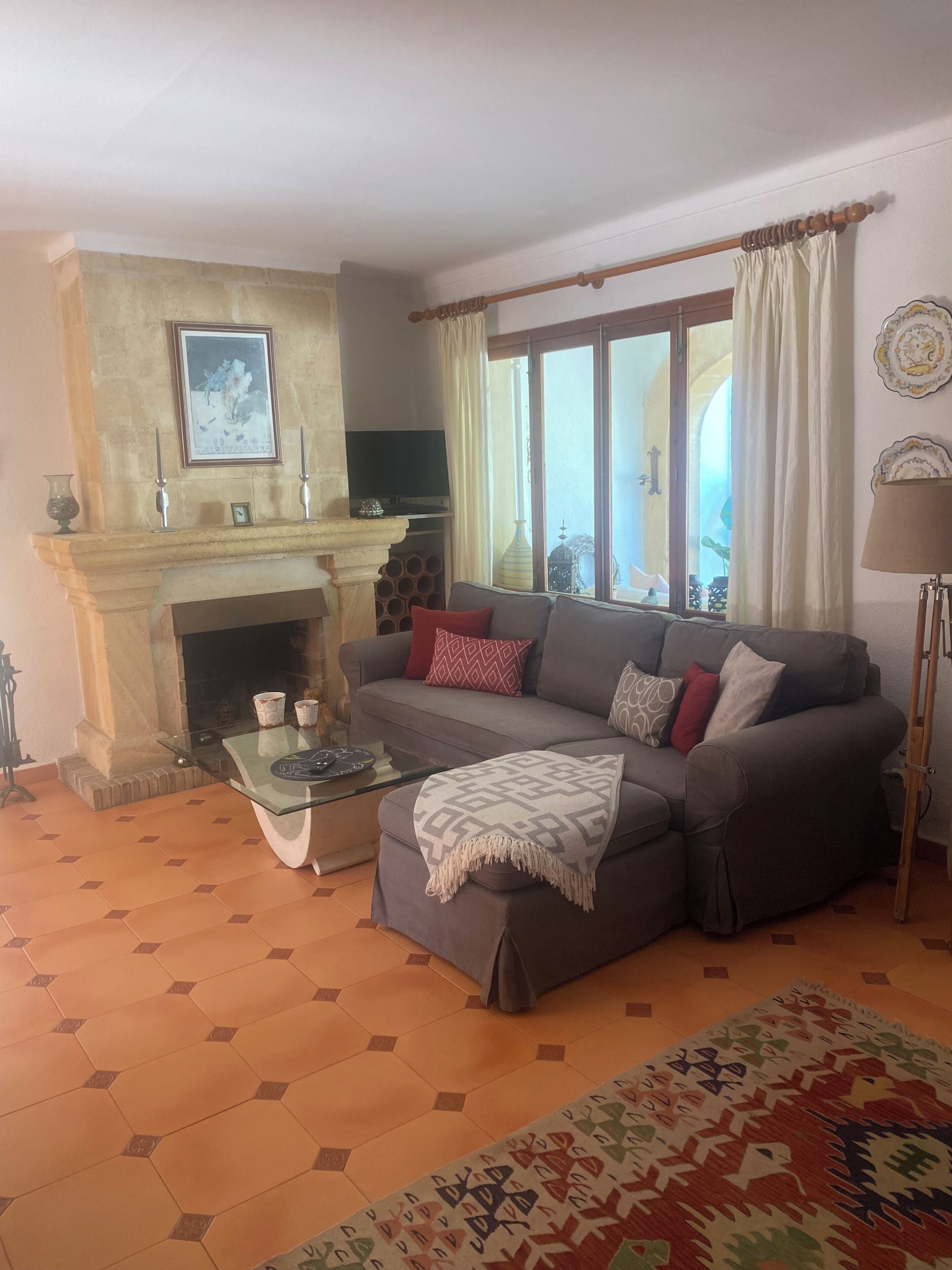 A living room with a sofa, a fireplace, a television, and a large window with curtains.