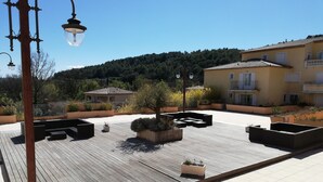 A rooftop terrace with wooden decking, planters with plants, and a clear view of the surrounding buildings and hills.