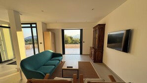 A modern living room with a teal sofa, wooden chairs, a small table, and a TV mounted on the wall. - Villa sea view in Pinarello - near Porto-Vecchio (ZONZA)