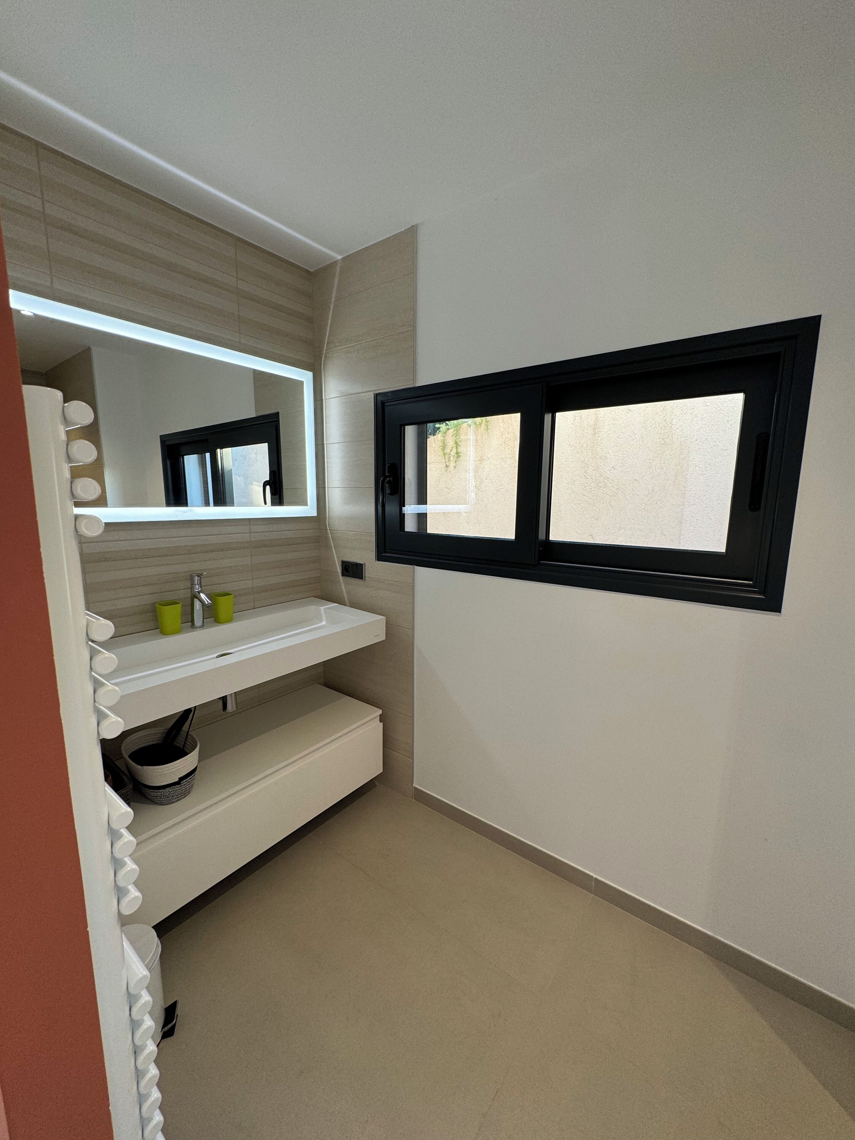 Une salle de bain moderne avec un meuble-lavabo blanc, un miroir et une fenêtre.