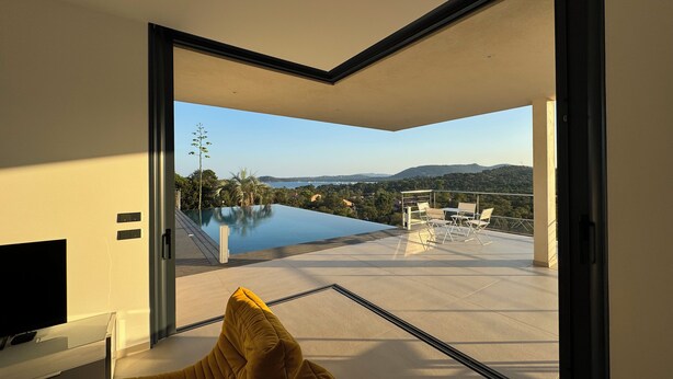 A modern living room with a large glass door leading to a balcony with a pool and a scenic view. - Villa sea view in Pinarello - near Porto-Vecchio (ZONZA)
