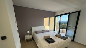 A modern bedroom with a large bed, a bedside table with a lamp, and a view of the outdoors through a sliding door. - Villa sea view in Pinarello - near Porto-Vecchio (ZONZA)