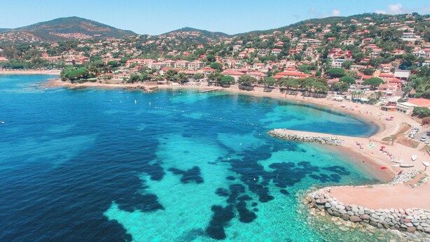 Uma cidade costeira com águas azul-claras, uma praia arenosa e edifícios com telhados vermelhos.