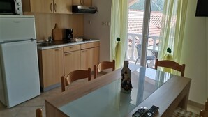A compact kitchen with wooden cabinets, a white refrigerator, and a dining table with chairs. There are two mobile phones on the table. - Apartment in Lopar with Terrace, Air condition, WIFI (4620-3) (Lopar)