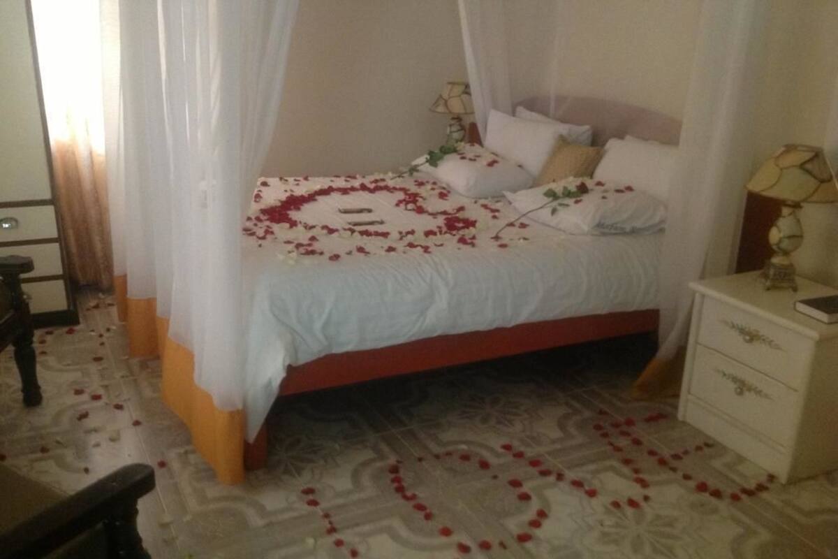A bed with a canopy, a bedside table with a lamp, and a patterned floor.