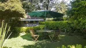 A patio with a table and chairs, a green umbrella, and a building in the background. - Lanet Matfam Resort (Nakuru)