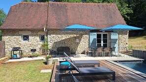 Une maison en pierre avec une piscine, du mobilier d’extérieur et un espace barbecue.