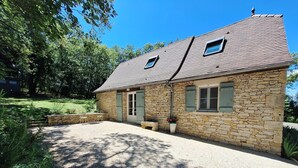A stone house with a gravel driveway, a small patio with a table and chairs, and a garden area.