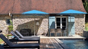 A stone building with a pool, outdoor seating, and blue umbrellas.