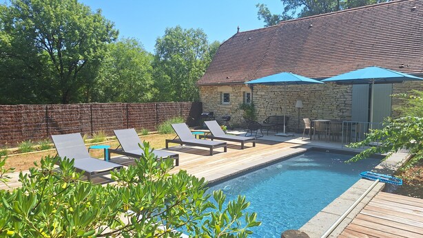 A backyard with a swimming pool, lounge chairs, a stone building, and a wooden deck.