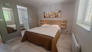 Une chambre à coucher avec un lit, un grand miroir, une fenêtre et une œuvre d’art accrochée au mur.