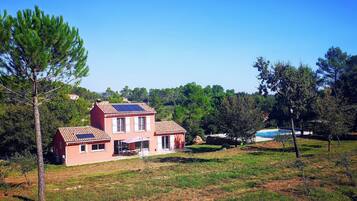 Une maison à deux étages, avec un toit en tuiles, des panneaux solaires et une piscine à l’arrière-plan.