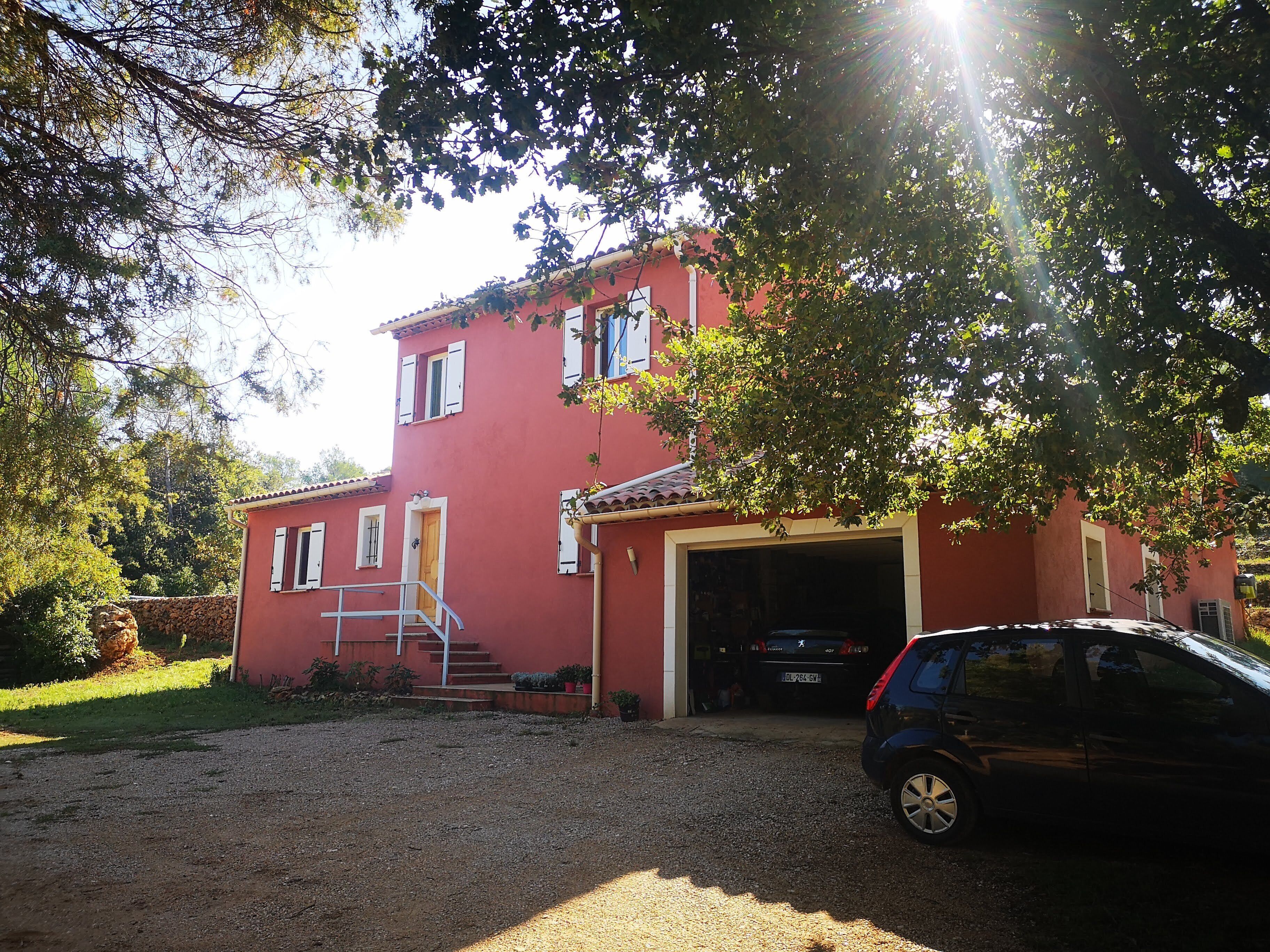 Un edificio rojo con garaje, camino de grava y un coche estacionado.