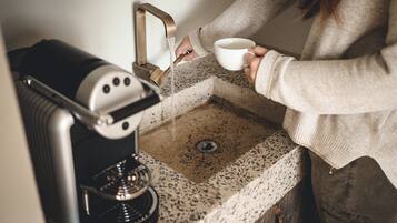 A person using a coffee machine near a sink with a speckled countertop.