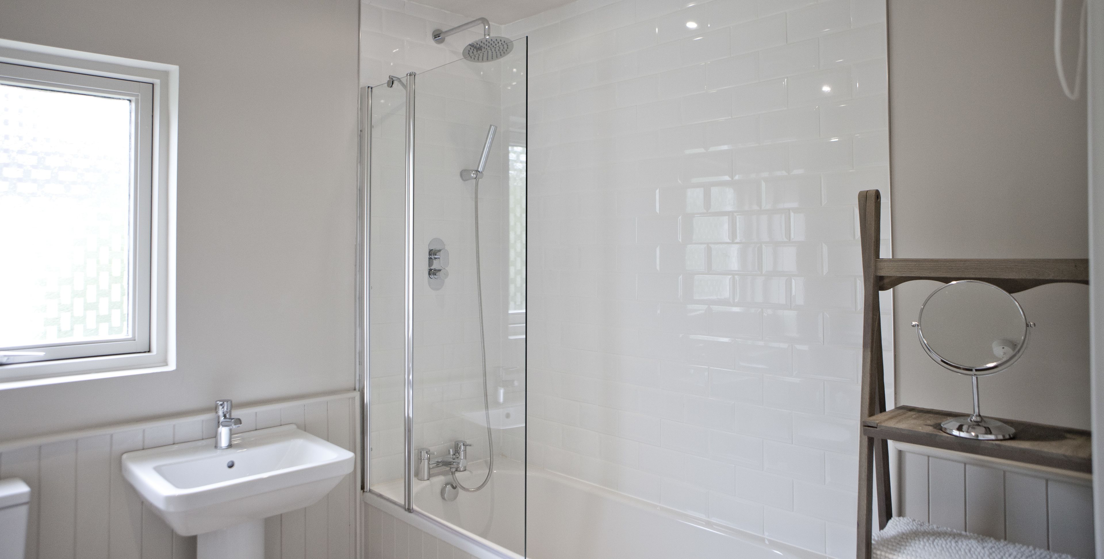 A bathroom with a glass-enclosed shower, a sink, and a mirror on a wooden shelf.