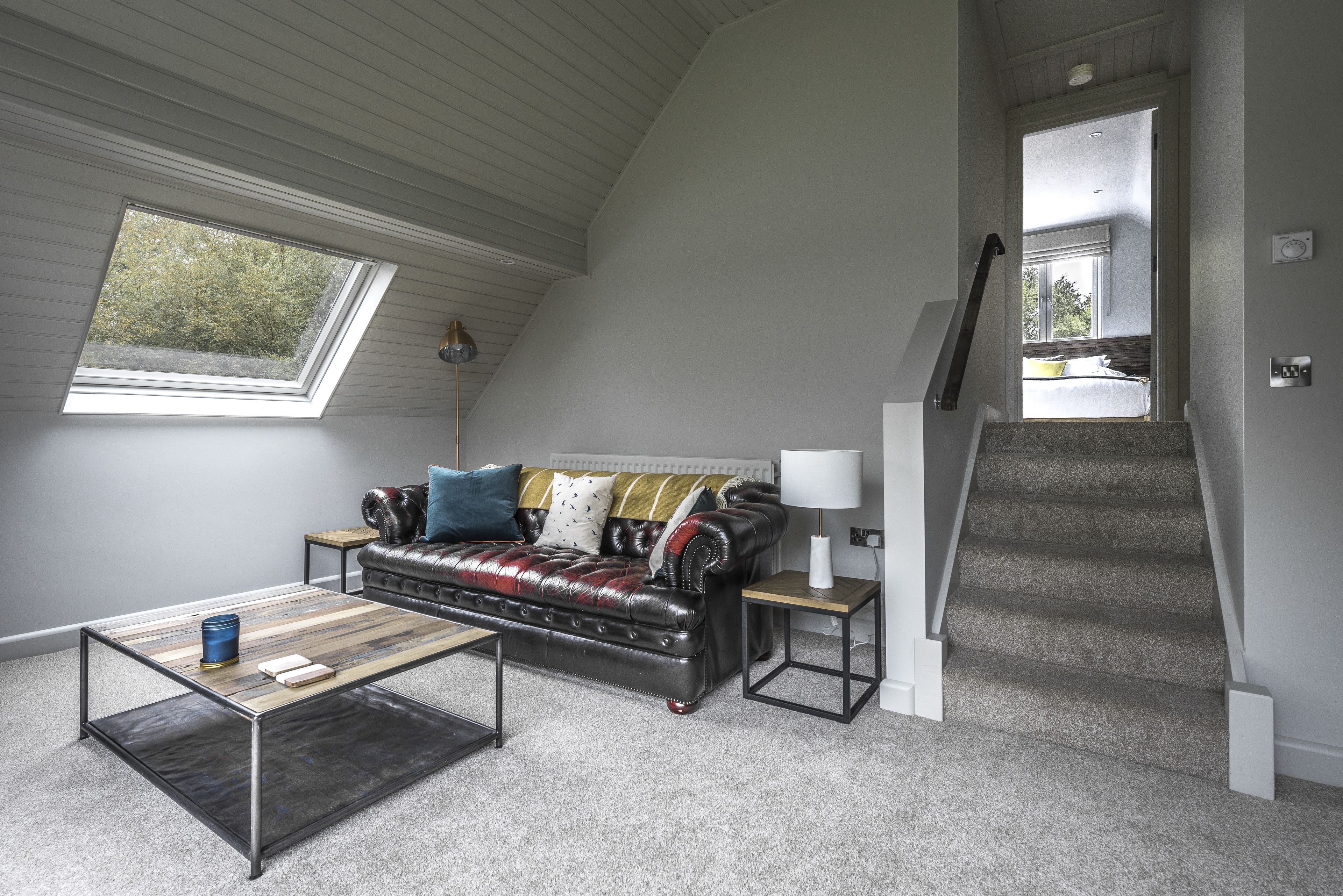 Un espacio tipo loft con techo inclinado, un sofá de cuero, una mesa de centro, una lámpara y una escalera que conduce a un nivel superior.