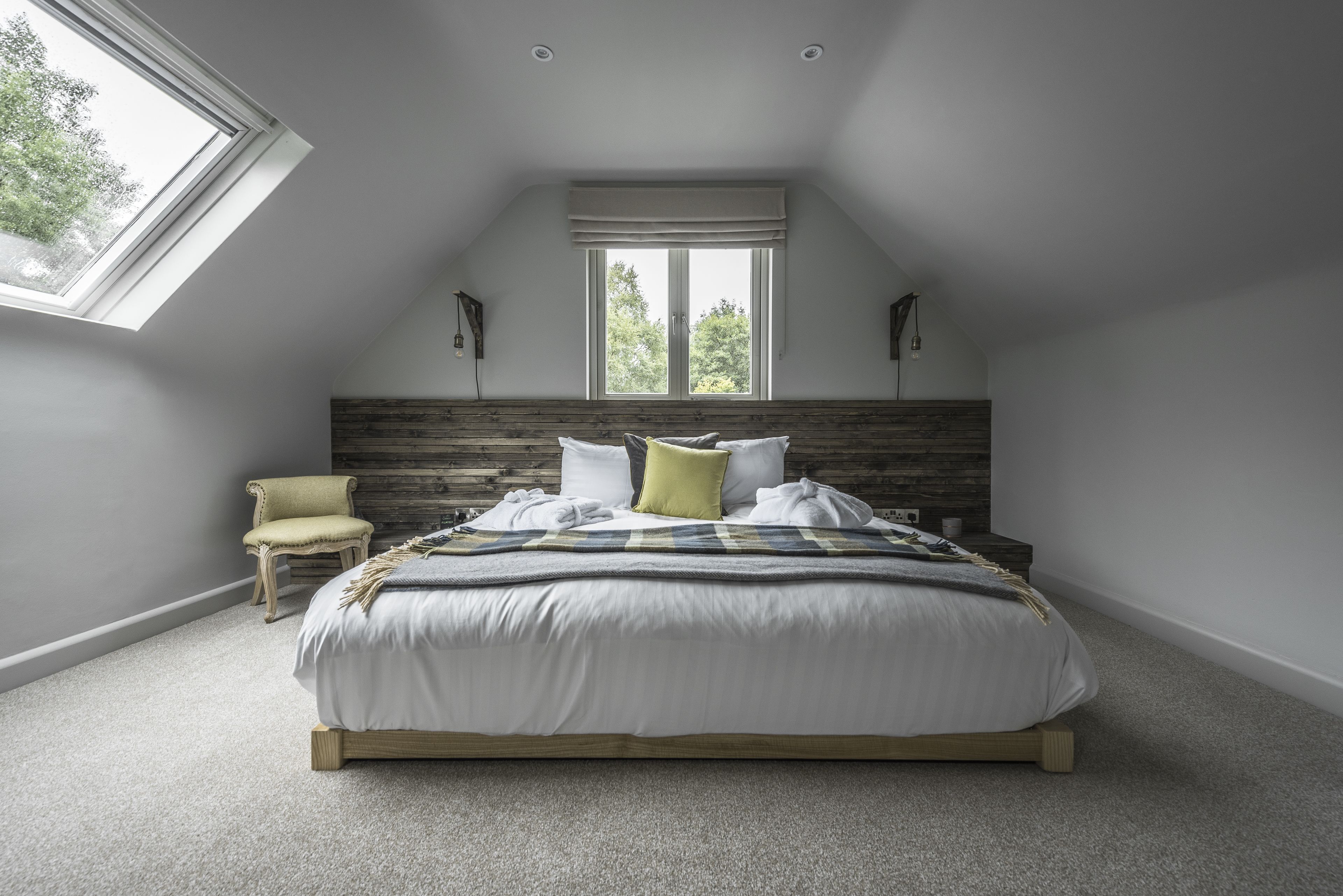 Een slaapkamer met een schuine kap, een groot bed, een stoel en een raam met uitzicht op bomen.