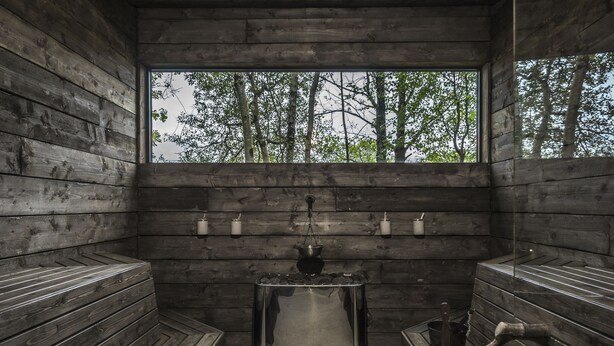 Una sauna con bancos de madera y una mesa central, ventanas amplias y vistas a árboles.