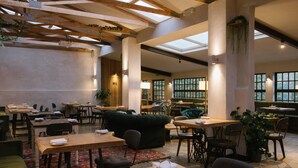 Un restaurante espacioso con techos altos, vigas de madera y ventanas amplias. Las mesas y sillas están dispuestas para comer.