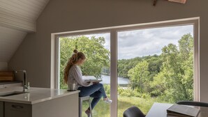 Una cocina moderna con un ventanal grande, un área de comedor con mesa y sillas, y vistas a un lago y un bosque.