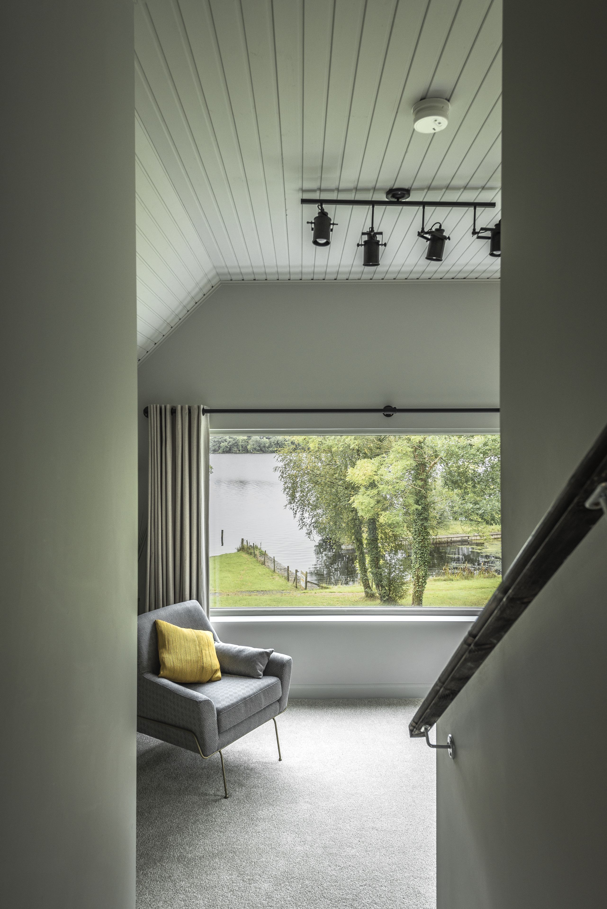 Una camera moderna con una grande finestra, un divano grigio con un cuscino giallo e un soffitto con illuminazione a incasso.