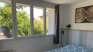 A bedroom with a bed, a window, a radiator, a wall-mounted plant, and a world map artwork. - Quai Ouest: 2/4p rental 100m from Goldbeach beach (Ver-sur-Mer)
