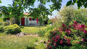 Een huis met een rode deur, een tuin vol roze bloemen en een houten terras.