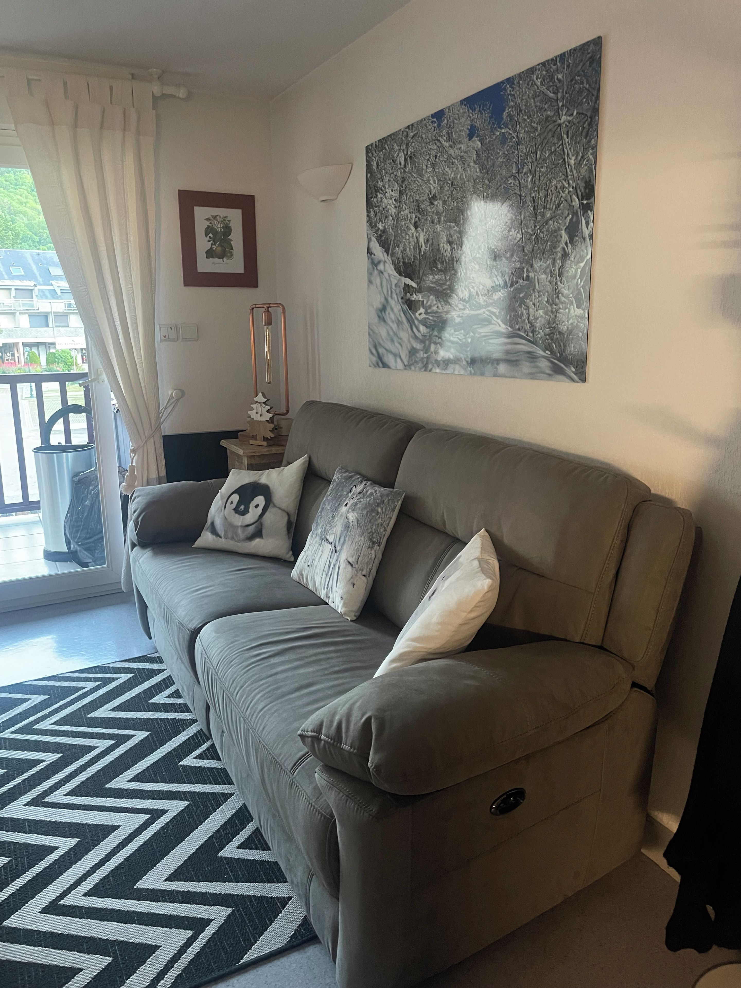 A living room with a sofa, a patterned rug, a painting, and a window with curtains.