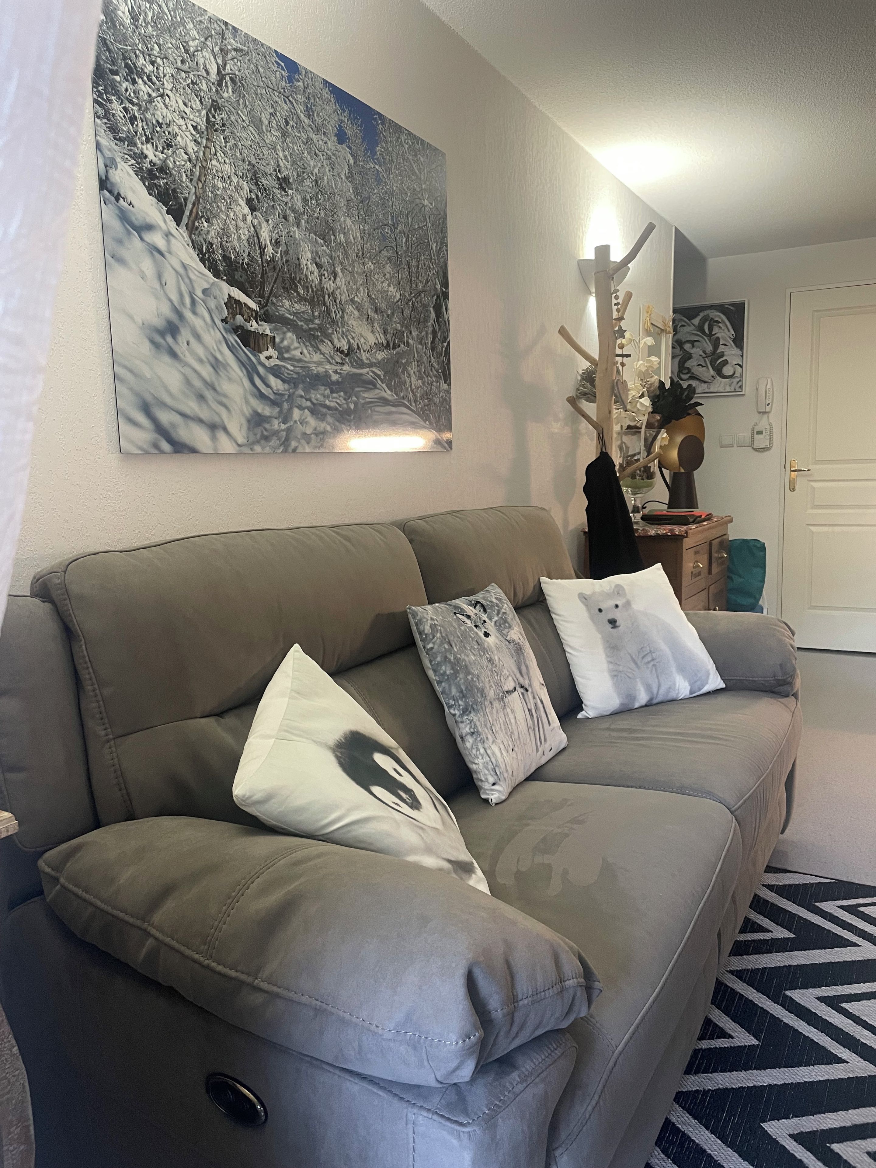Sala de estar com sofá cinza, uma pintura grande com tema de inverno e tapete estampado.