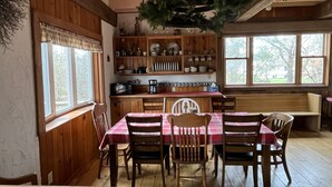 A cozy dining area with a wooden table and chairs, a hanging plant, and a kitchen with wooden cabinets and a window. - In-Town Moose Haus Lodge  (Clear Lake)