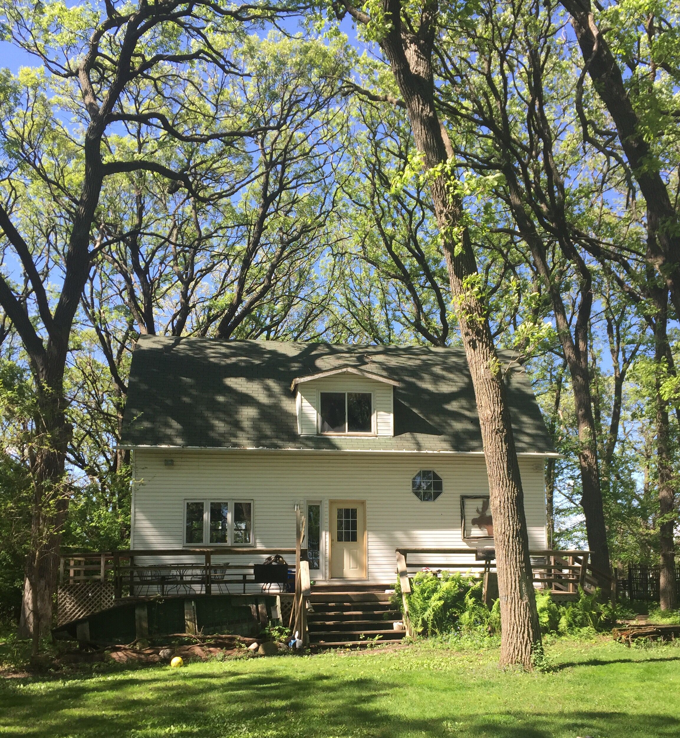 A two-story house with a front porch, surrounded by trees.