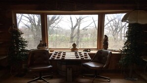 A cozy room with a large window, two chairs, a chessboard, and a small statue. - In-Town Moose Haus Lodge  (Clear Lake)