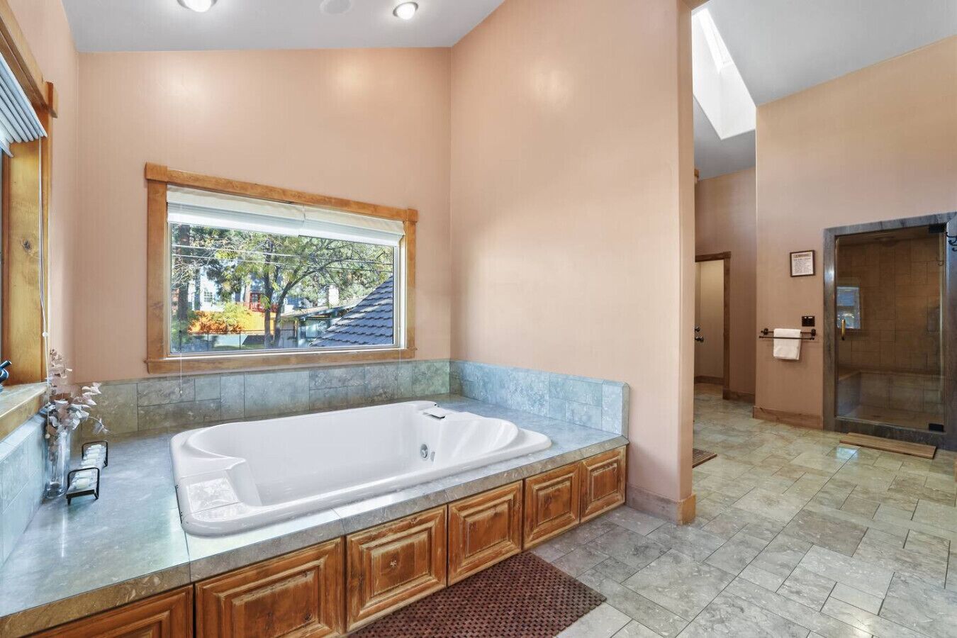 A spacious bathroom with a large bathtub, wooden cabinetry, a window with a view, and a shower area.