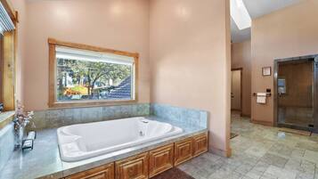 A spacious bathroom with a large bathtub, wooden cabinetry, a window with a view, and a shower area.