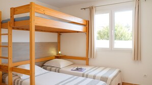 Une chambre avec un lit superposé, comprenant deux lits, une fenêtre avec des rideaux et une table de chevet avec une lampe.