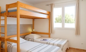 A bunk bed room with two beds, a window with curtains, and a bedside table with a lamp.